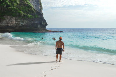 Rear view of shirtless man standing at beach against sky