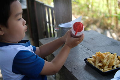 Boy holding bottle of sauce over food at table