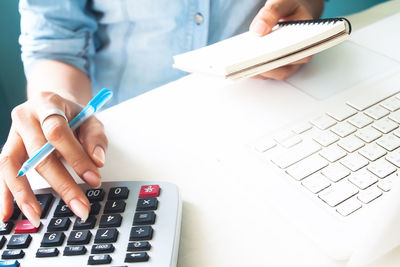 Midsection of woman using calculator with laptop on table