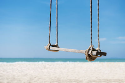 Close-up of swing hanging over sand at beach against sky