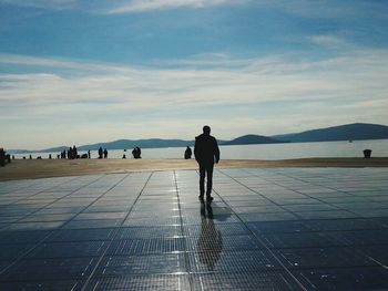 Rear view of man walking on sea against sky