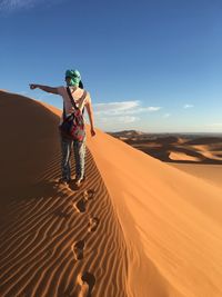 Woman on sand dune in desert against sky