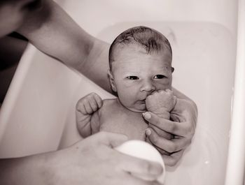 High angle view of woman bathing newborn baby boy in bathtub at home