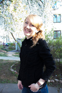 Portrait of young woman standing on tree trunk