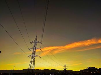 Low angle view of silhouette electricity pylon against dramatic sky