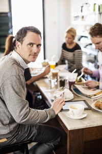Portrait of mid adult businessman with colleagues having breakfast in office restaurant