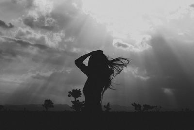 Silhouette woman on field against cloudy sky during sunny day