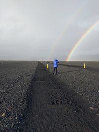 Rear view of person walking on road against rainbow in sky