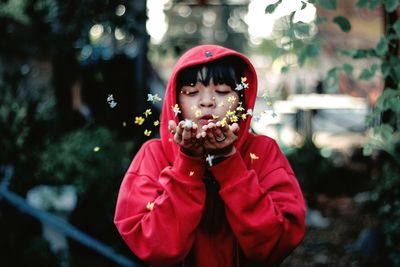 Girl wearing hooded shirt while blowing flowers