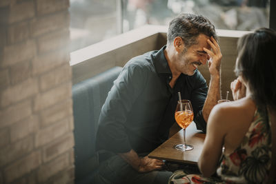 Happy man with drink sitting by girlfriend in restaurant