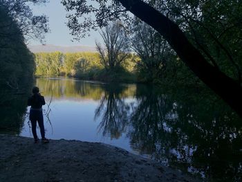 Rear view of people standing by lake in forest