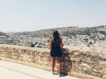 Rear view of woman looking at cityscape against clear sky