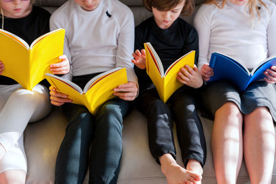 Four children sitting comfortably together on sofa in living room and doing prep work for school