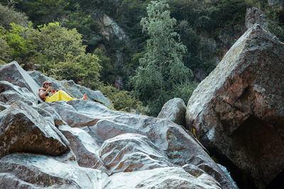 Man and woman sitting on rock in forest