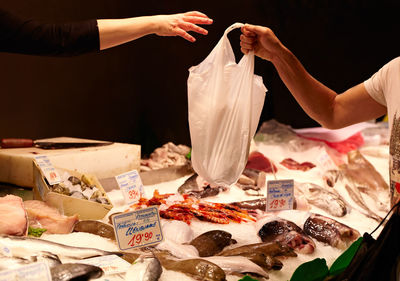 Cropped hand of vendor giving bag to customer over fishes on sale at market