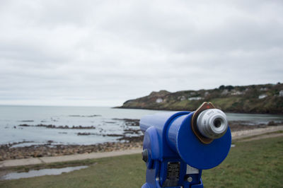 Close-up of coin-operated binoculars on beach against sky