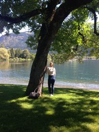 Rear view of woman standing by tree against lake