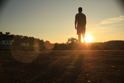 Rear view of silhouette man standing on landscape against sunset sky