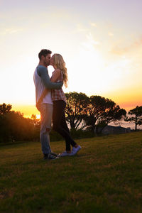 Side view of woman standing on field against sky during sunset