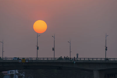 Silhouette bridge over street against orange sky