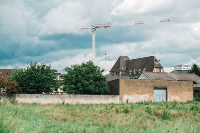 Construction crane by building and trees against sky