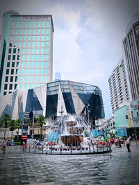 People in front of modern buildings in city against sky