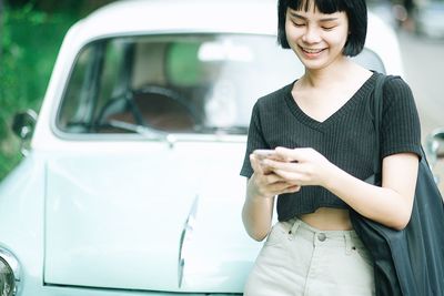 Young woman using phone while standing by car