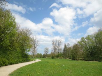 Road passing through field against cloudy sky