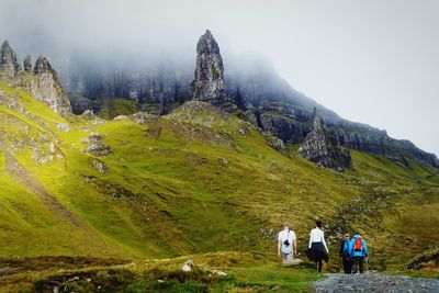 Tourists walking on grassy landscape in scotland, old man of storr