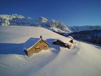 Houses on snowcapped mountain against clear blue sky