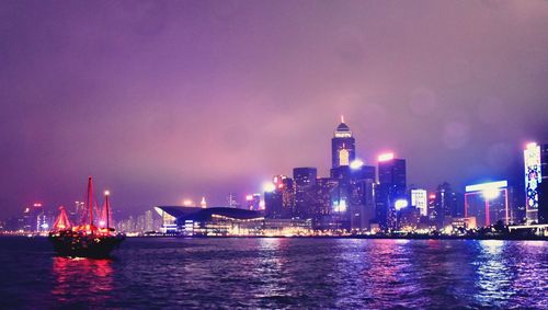 Illuminated buildings by sea against sky at night