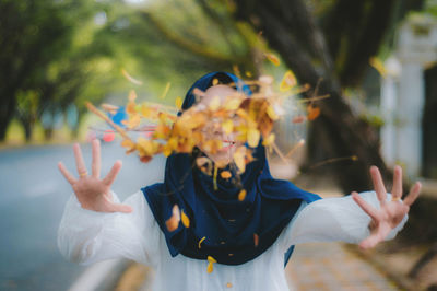 Portrait of happy young woman throwing autumn leaves on footpath