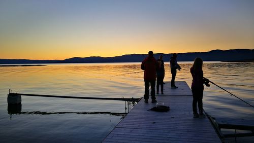 Silhouette people standing on pier over sea against clear sky during sunset