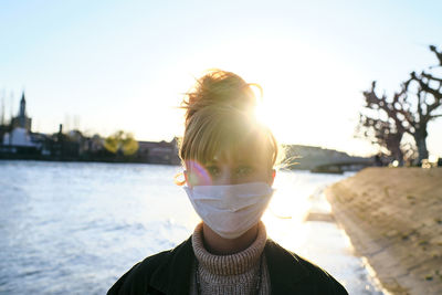 Portrait of woman wearing mask standing against lake