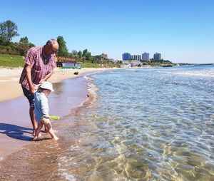 Man with grandson standing on shore at beach during sunny day