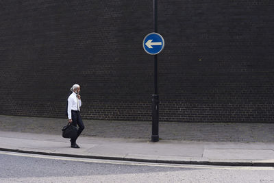 Elegant senior businessman with luggage walking on pavement in the opposite direction