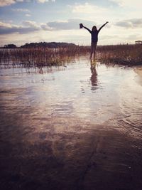 Girl with arms outstretched standing by lake against sky