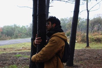 Side view of man standing by tree trunk in forest