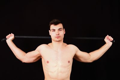 Portrait of shirtless young man holding equipment against black background