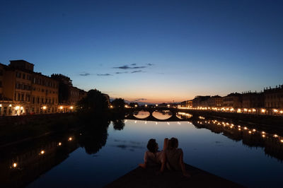 Rear view of man and woman sitting by river at dusk