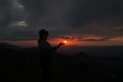 Optical illusion of woman holding sun while standing on mountain against orange sky