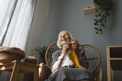 Happy senior woman knitting on chair in living room