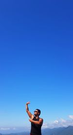 Man gesturing while standing against blue sky