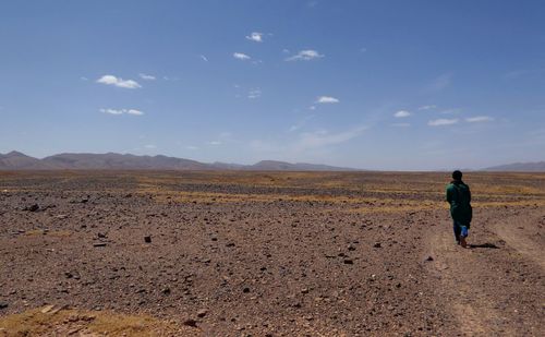 Full length rear view of male guide walking at desert against blue sky