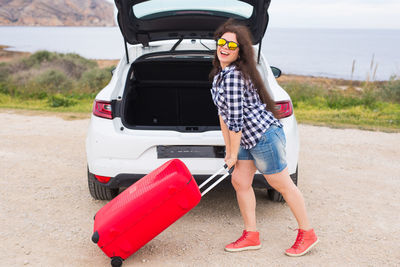 Full length portrait of young woman standing on car