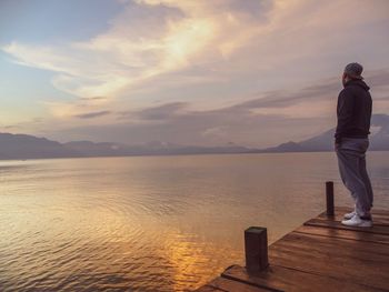 Full length of man standing on pier over lake against sky during sunset