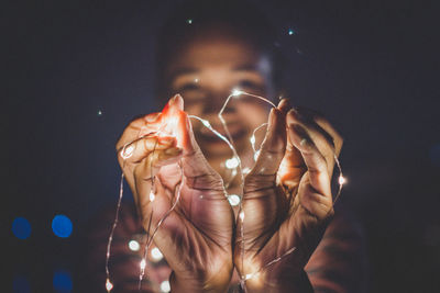 Cropped image of woman holding illuminated string light at night