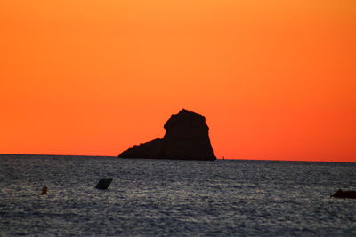 Rock formation in sea against romantic sky at sunset