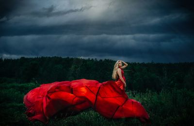 Woman with red umbrella on field against sky