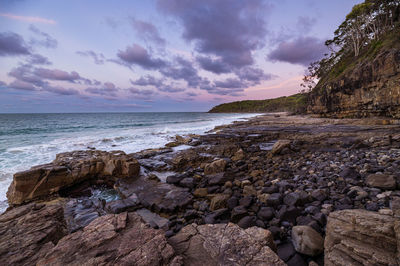 Rocks on beach against sky during sunset